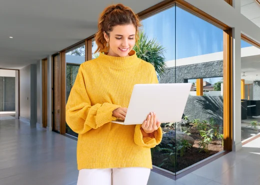 Mulher sorridente usando notebook em saguão moderno. Gestão profissional de aluguel por temporada pela Casa Hotel Assessoria.